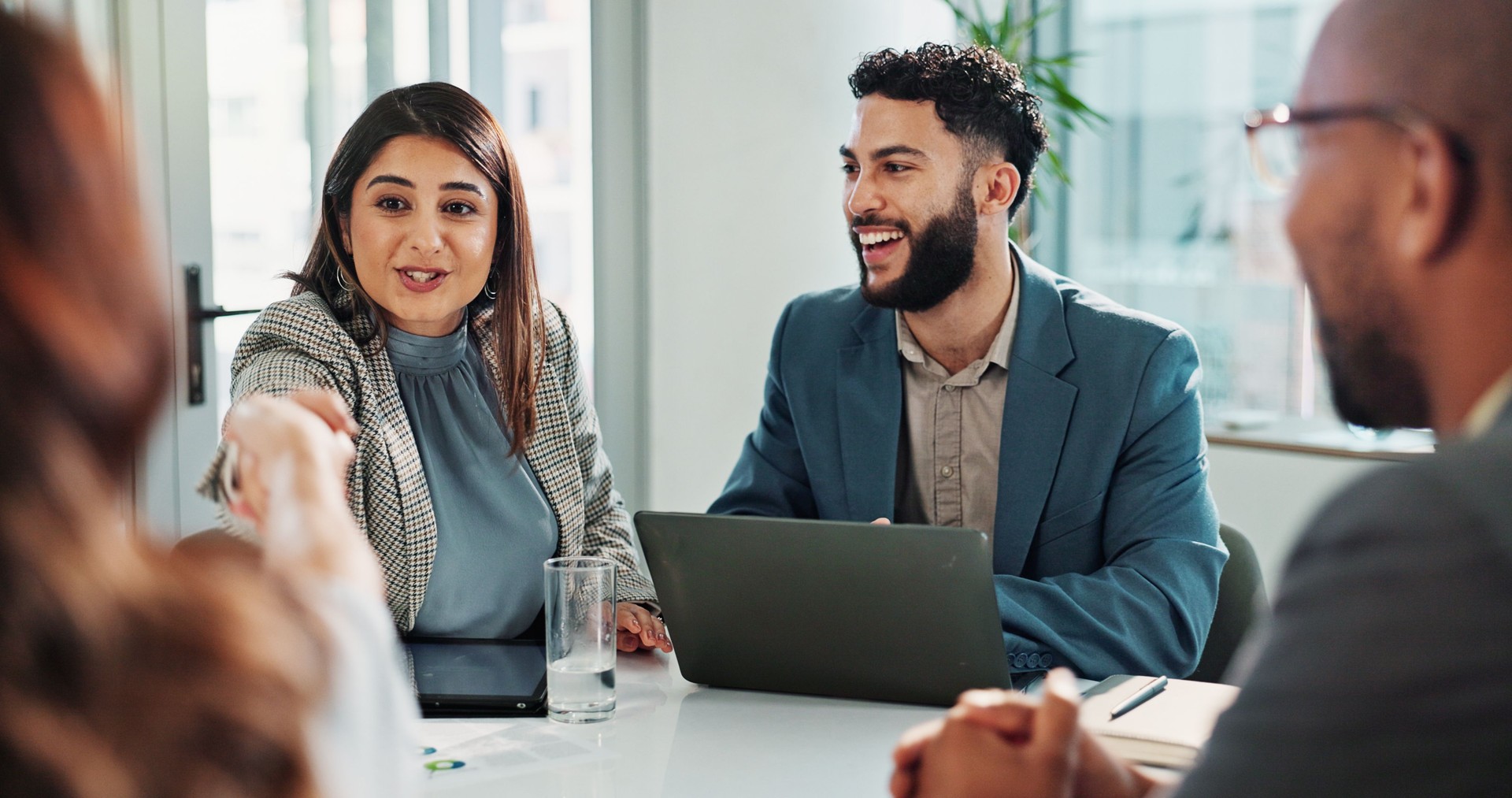 Happy, business people and laptop with handshake in meeting for deal, agreement or collaboration at office. Group, employees or colleagues shaking hands at conference for teamwork or introduction